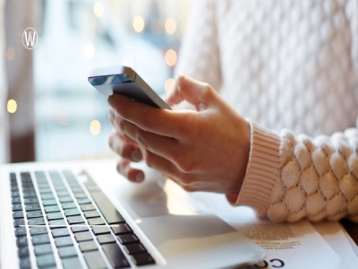 شخص يستخدم هاتفًا محمولًا، وأمامه حاسوب محمول. يرتدي سترة بيضاء،