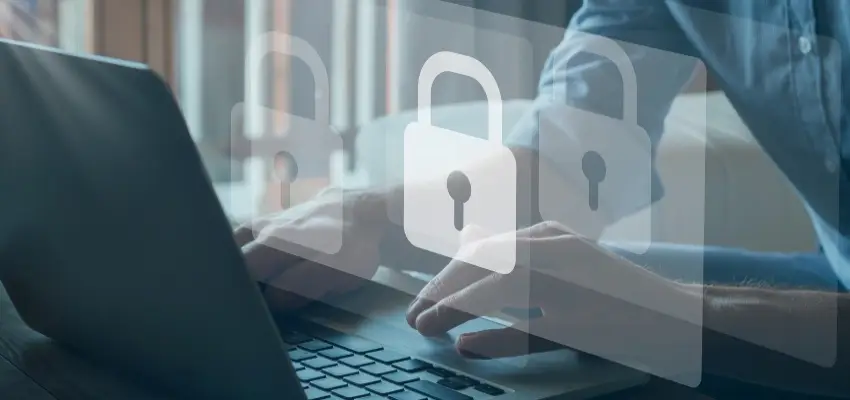 يظهر جهاز كمبيوتر محمول، يُفترض أنه مُشغّل ببرنامج أمان، مع وضع يدي المستخدم على لوحة المفاتيح. أيقونات قفل مُركّبة، مما يُرجّح أنه يُشير إلى حماية البيانات.