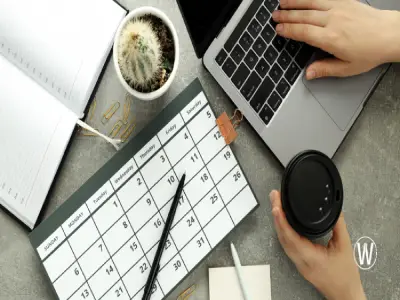 يحتوي المكتب على جهاز كمبيوتر محمول، وتقويم، ودفتر ملاحظات مفتوح، وفنجان قهوة، ونبتة صبار. ويُظهر التقويم أيام الأسبوع مطبوعة بالأرقام من 1 إلى 31.