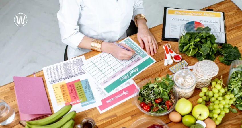 شخص ما يخطط لجدول وجبات رمضان مع قائمة مشتريات ذكية، يتضمن الخضراوات والفواكه، ولديه خطة وجبات جاهزة. توجد ورقة مكتوب عليها "نسب المغذيات الكبرى: 45-65% كربوهيدرات، 10-25% بروتين".