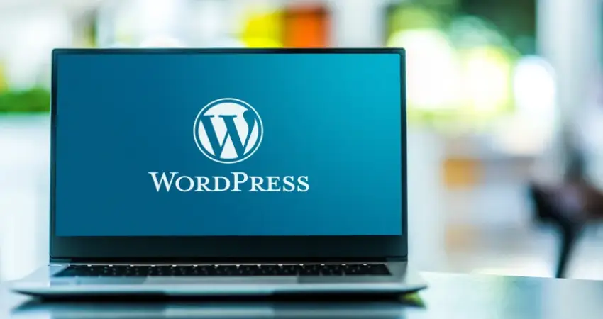 لابتوب مفتوح، في منتصف الصورة، يظهر شاشة اللابتوب بشعار WordPress، مكتوب تحته كلمة WordPress باللون الأبيض. الشاشة زرقاء. اللابتوب على طاولة تعكس بعض الضوء. خلفية الصورة ضبابية، تظهر ألوانًا متداخلة من الأبيض والأخضر والأصفر، مما يشير إلى بيئة داخلية أو خارجية غير محددة. الإضاءة طبيعية، والظلال خفيفة، مما يعطي جوًا هادئًا. الزاوية منخفضة قليلًا، مما يركز على اللابتوب كعنصر رئيسي. اللابتوب في وضعية مفتوحة، مما يوحي بإمكانية استخدامه أو العمل عليه. التفاصيل واضحة، مع تركيز على شعار WordPress والكلمة المكتوبة.